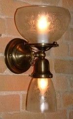 Brass wall sconce with two frosted glass shades, illuminating a brick wall.
