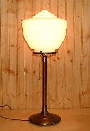 A vintage table lamp with a cream-colored, ribbed glass shade and bronze base, cord visible.
