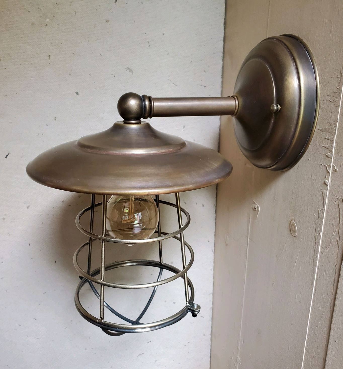 Bronze wall-mounted light fixture with a cage-like shade and exposed bulb, mounted on a light-colored wall.