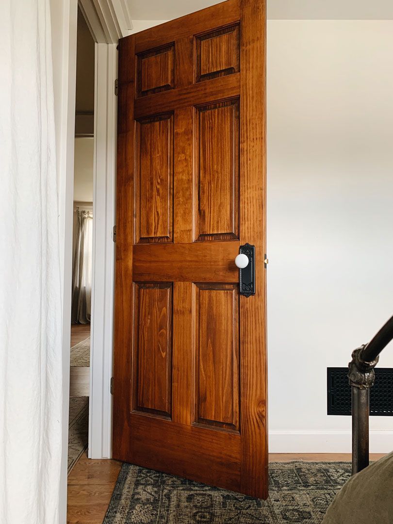 Wooden door slightly ajar, revealing a hallway. Door has black hardware and white knob.