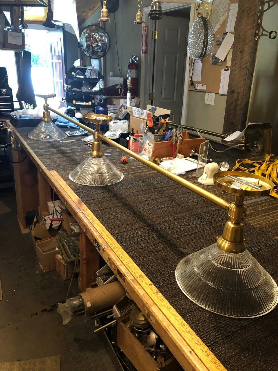 Three brass and glass lamps on a workbench, likely for repair. Shop setting with tools and parts visible.