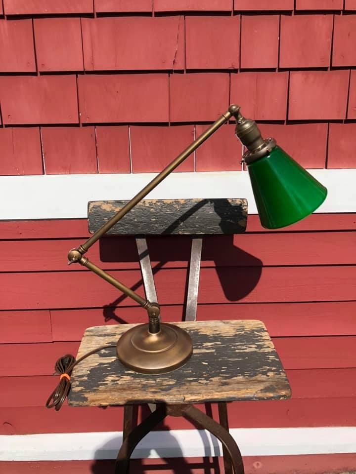 Vintage brass desk lamp with green glass shade, on a weathered stool against a red wall.
