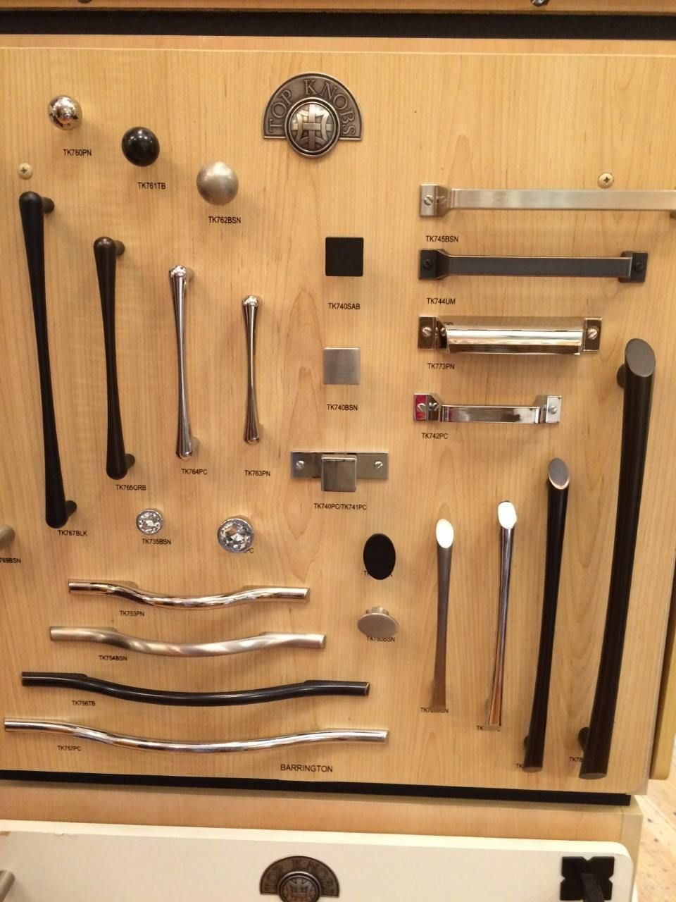 Display of various cabinet knobs and pulls on a wooden board for home design.