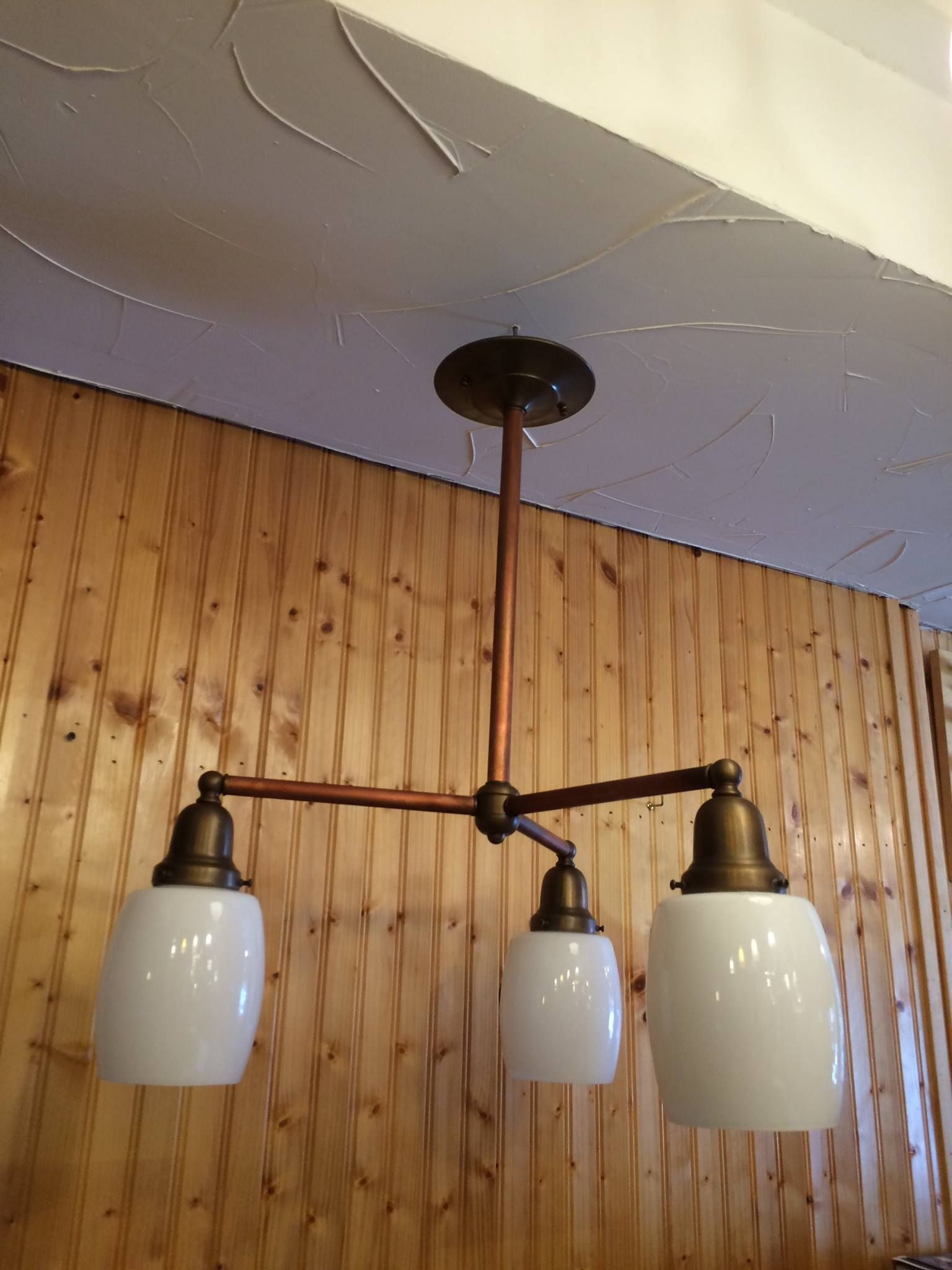 Three-light ceiling fixture with white globe shades and copper-colored arms, mounted against wood paneling.