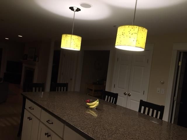Kitchen island with two yellow pendant lights, fruit, and black chairs. Dark setting.