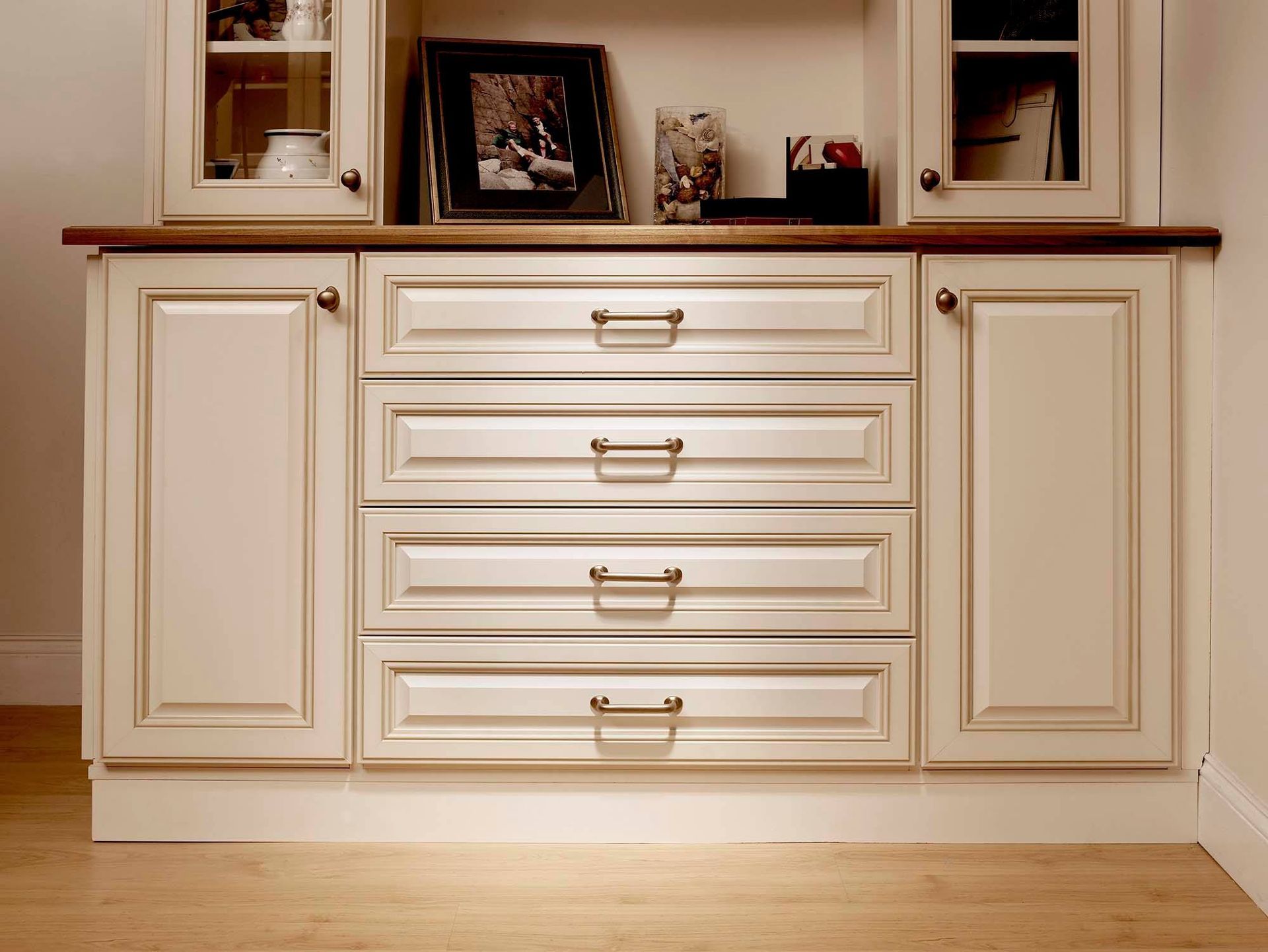 Cream-colored kitchen cabinet with four drawers, two side doors, and a shelf displaying decor.