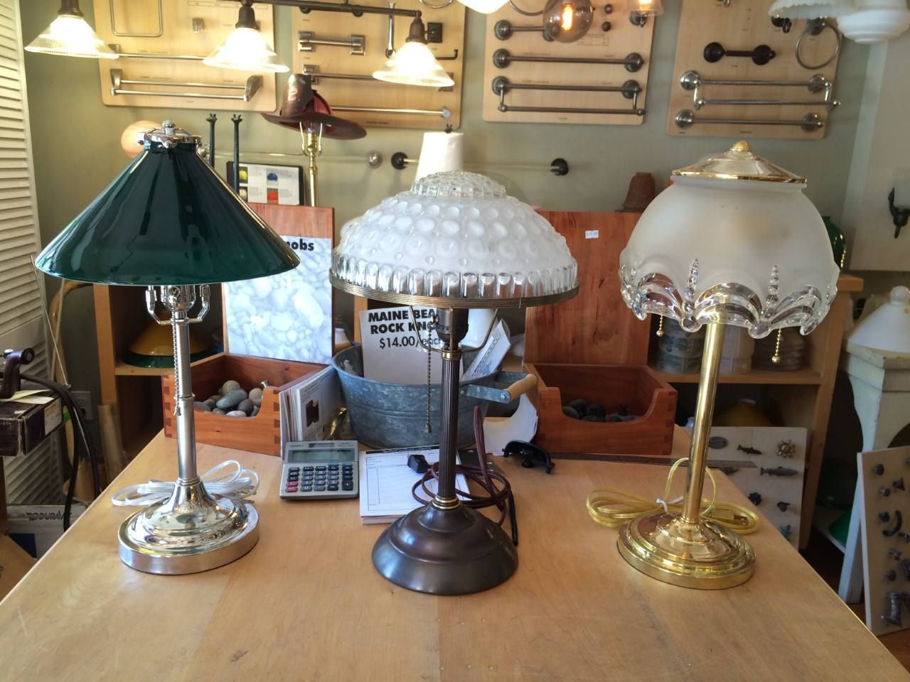 Three vintage lamps with ornate bases and glass shades on a wooden table in a shop.