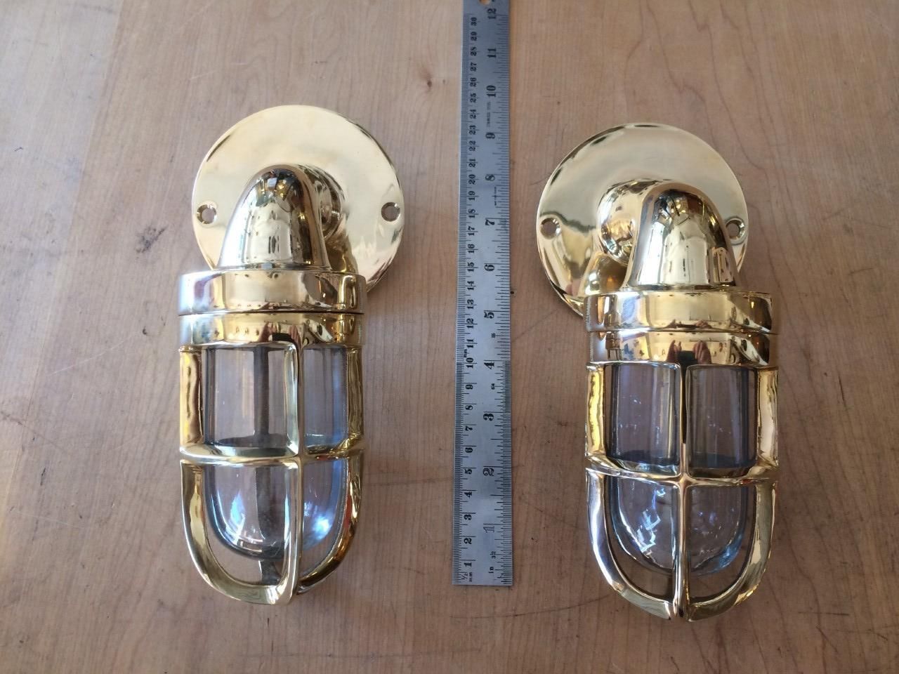Two brass-colored nautical-style wall lights with a ruler in between them on a wooden surface.