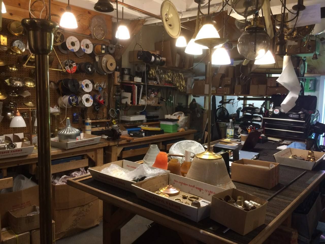 Workshop interior with tools, wires, lamps, and boxes. Wooden workbench in a cluttered space.
