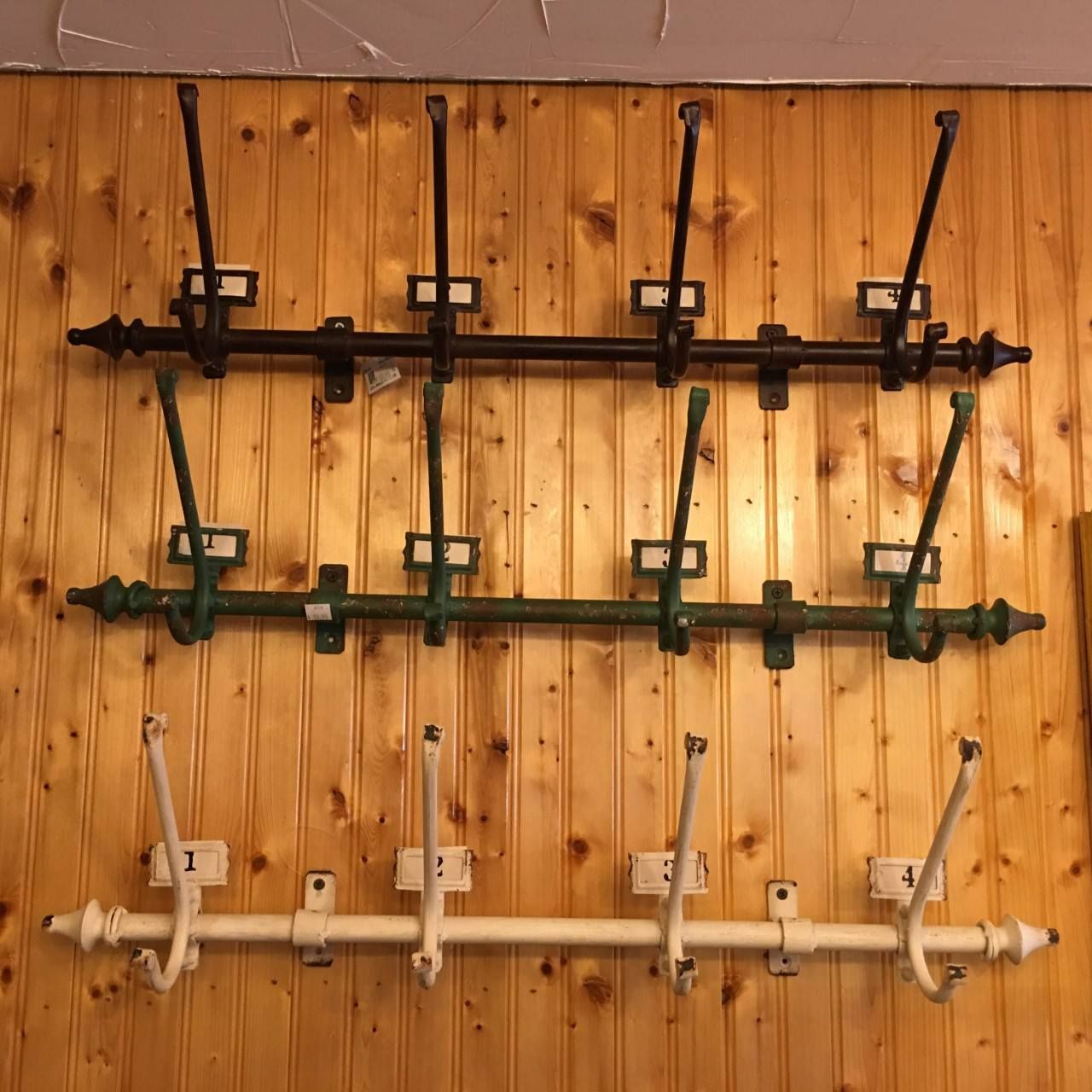 Three antique metal coat racks mounted on a wooden wall.