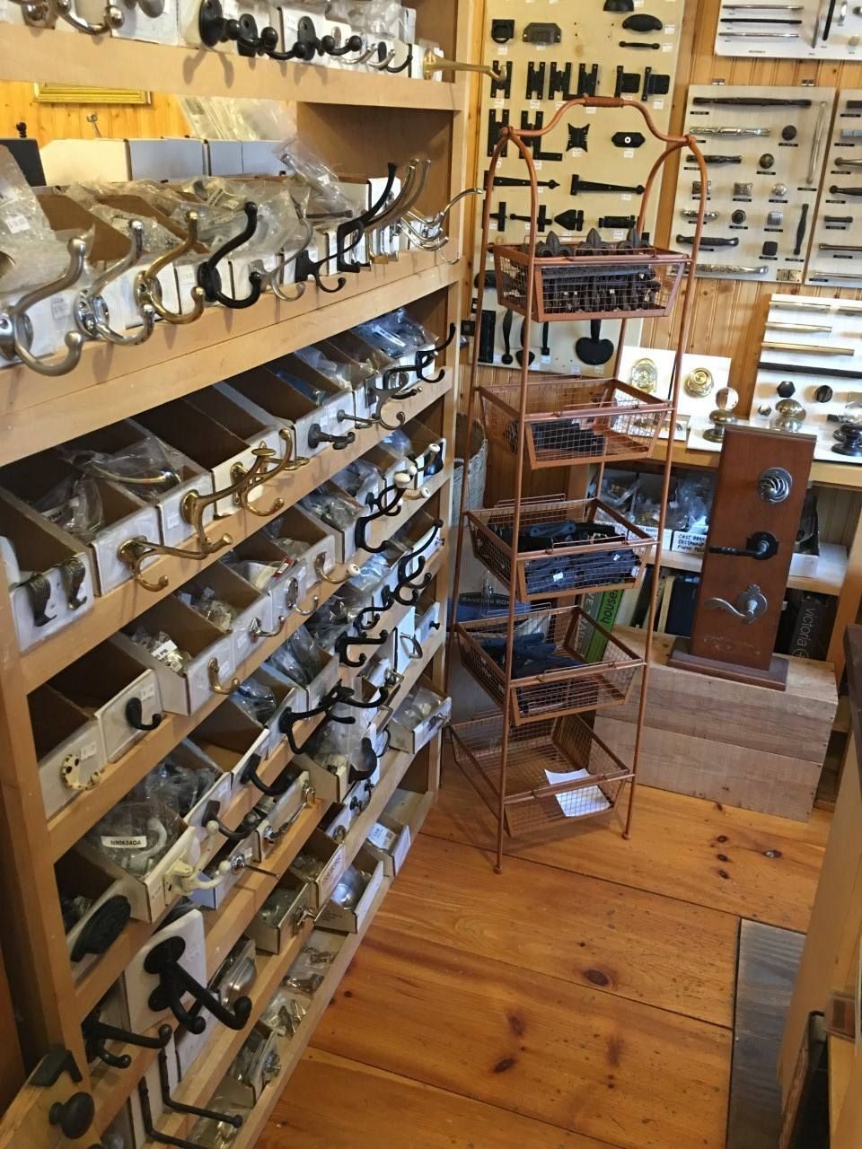 Shelves of cabinet hardware in a store, wooden floor and walls, metal display stand.