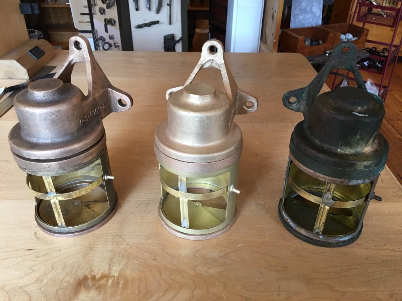 Three antique brass nautical lamps on a wooden surface, each with a different patina.
