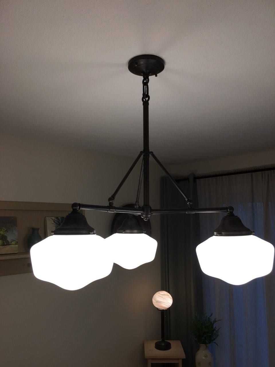 Black chandelier with three white, wavy-edged globe shades, hanging from a ceiling.