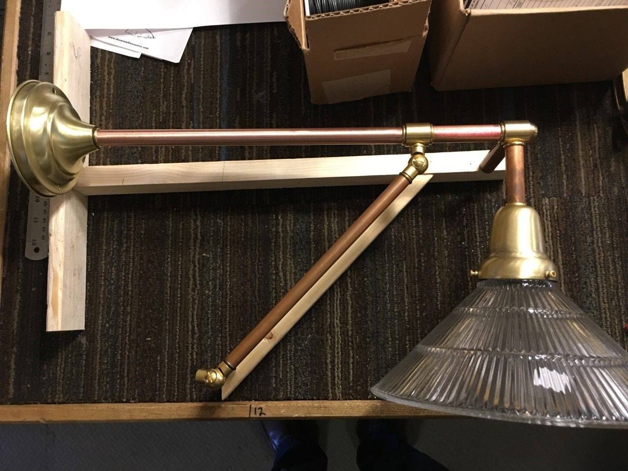 Brass and copper adjustable wall lamp with a ribbed glass shade, mounted on wooden supports.