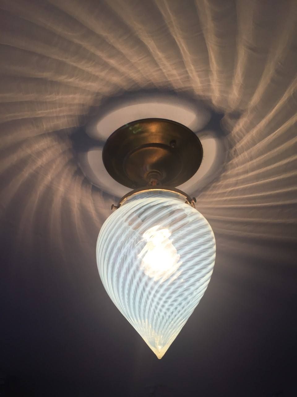 Ceiling light fixture with swirling white glass shade, casting a patterned shadow on the ceiling.