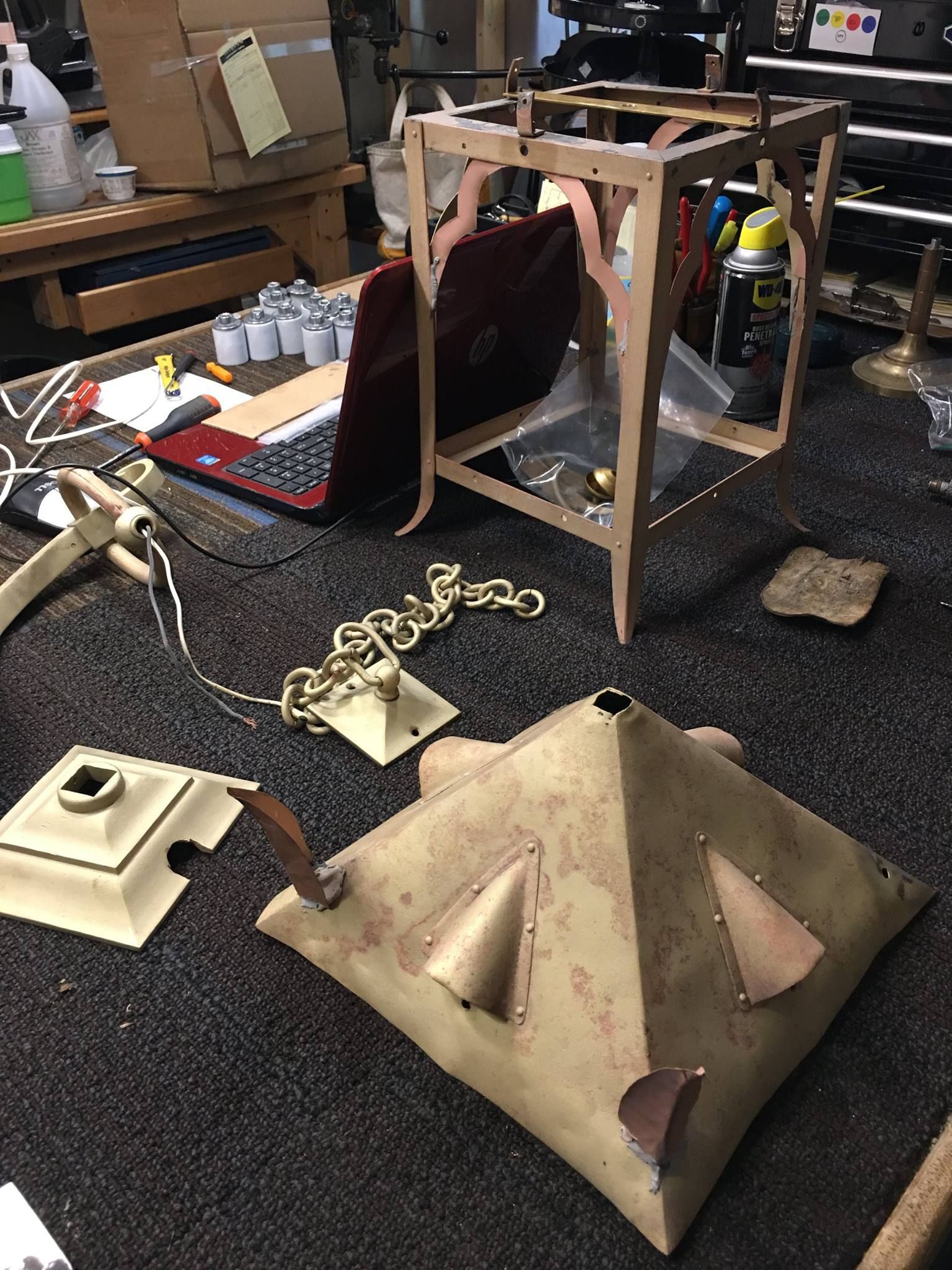 Workbench with ornate chandelier components in various stages of assembly, including chain, frame, and shade.