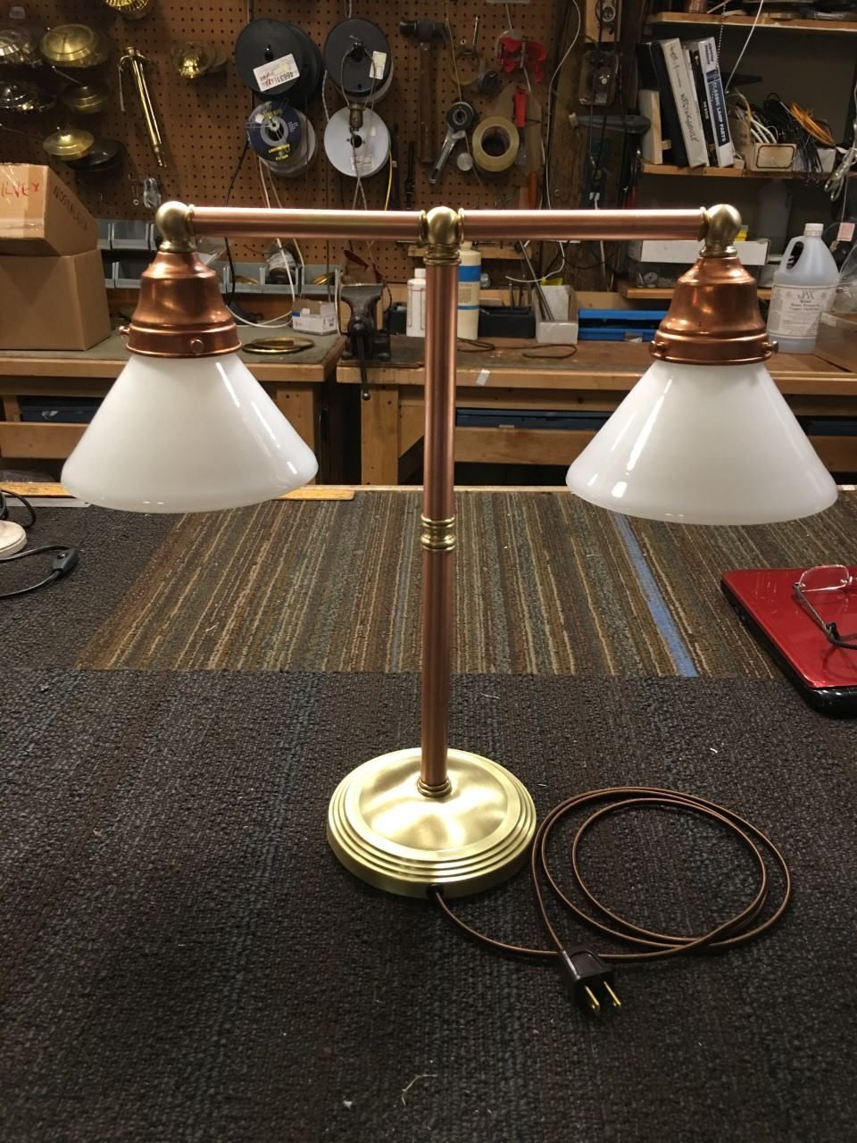 Copper and brass desk lamp with two white glass shades, on a work surface.