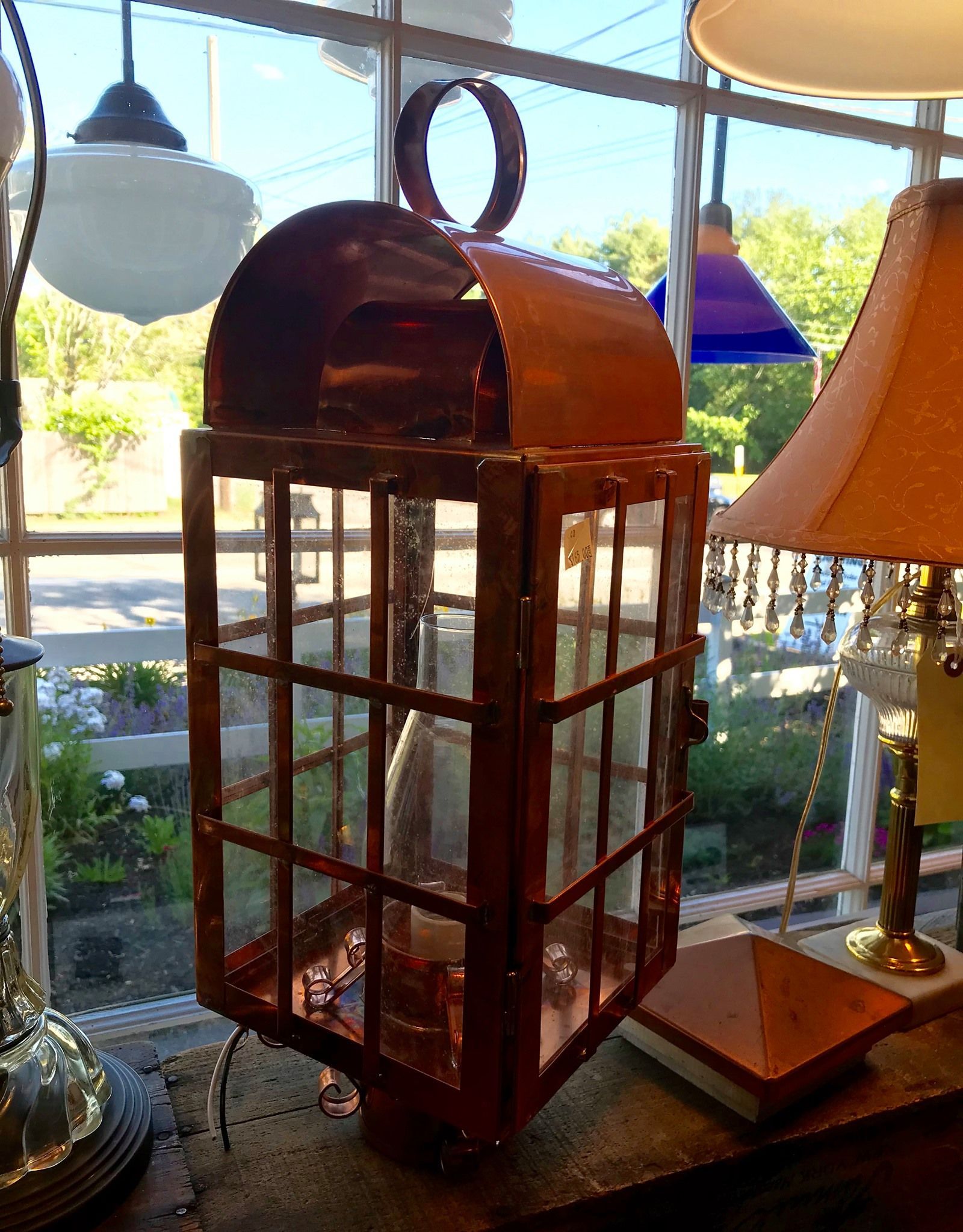 Copper lantern with glass panels, a curved top, and a hanging loop, inside a shop.