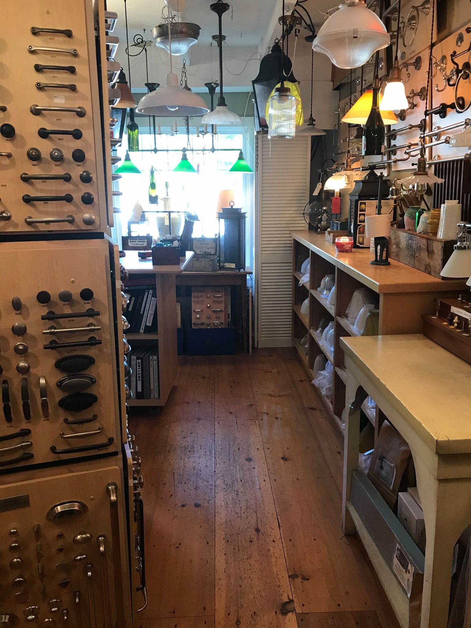 Interior view of a hardware store aisle with wood floors, shelves, and various light fixtures.