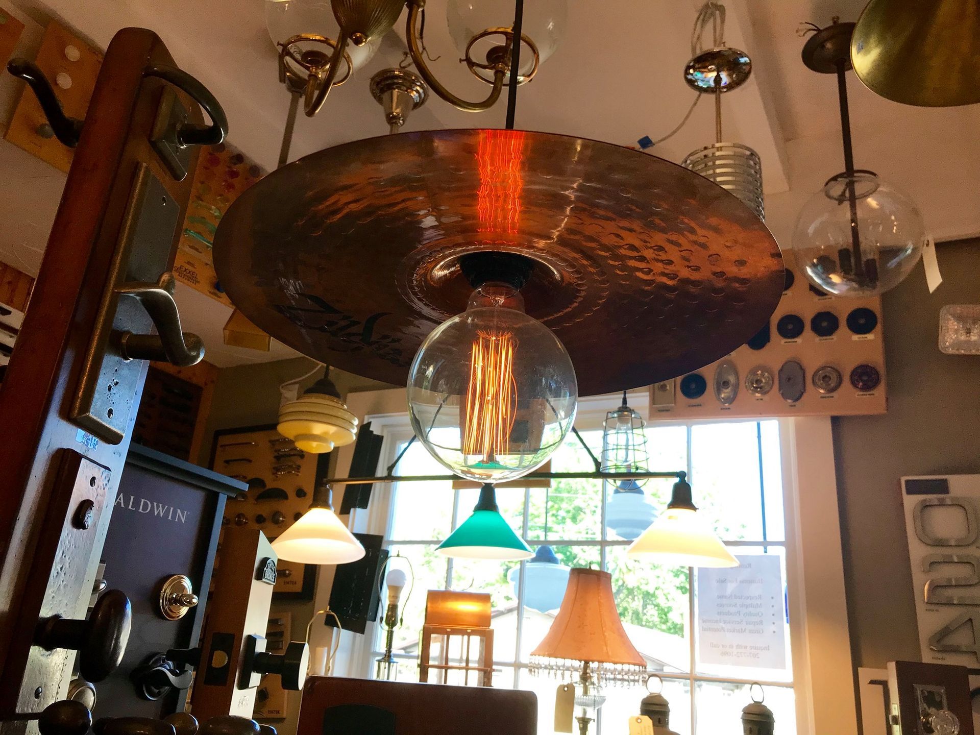 A ceiling light fixture with a large cymbal shade and a vintage bulb, inside a shop.