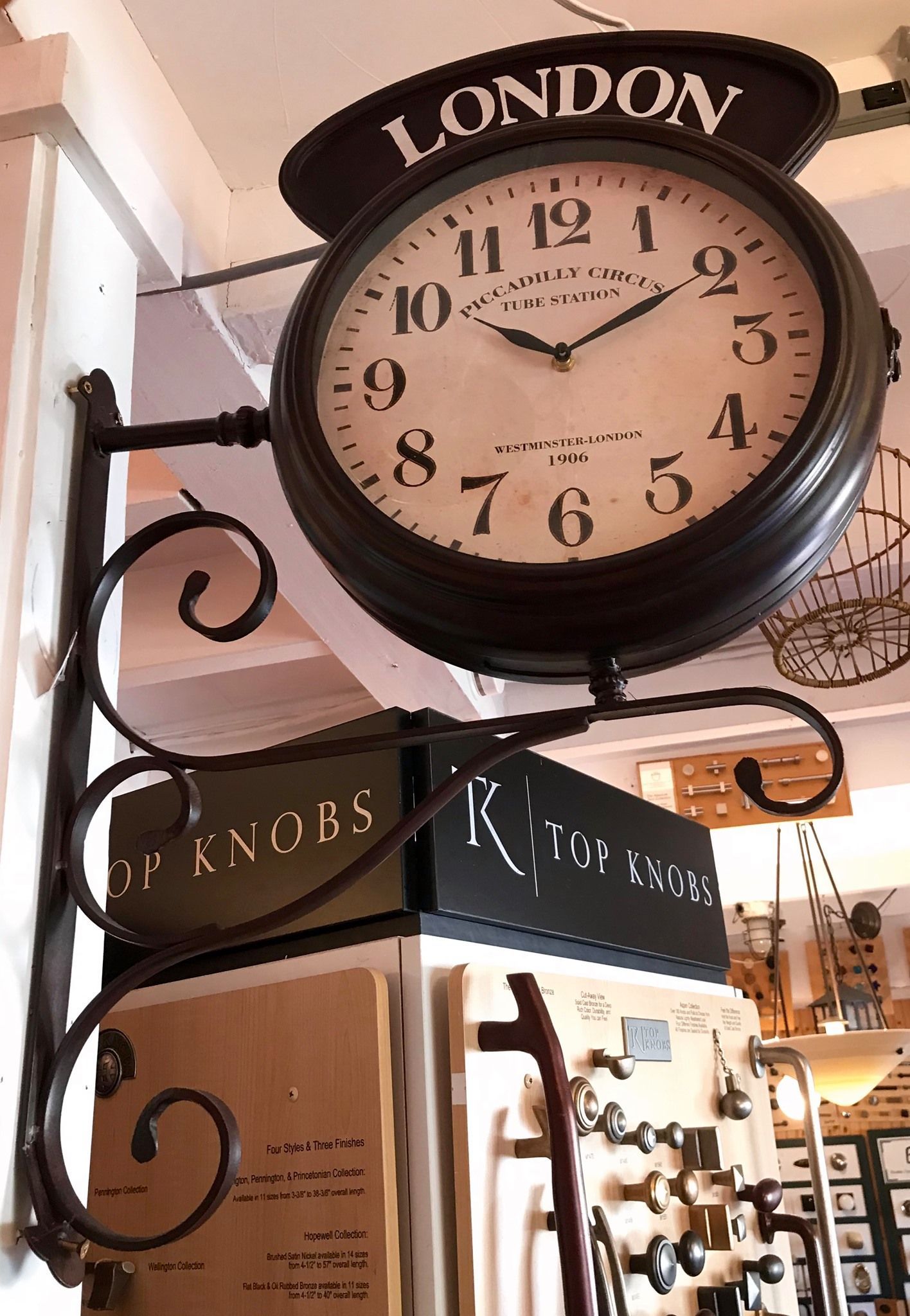 Double-sided London clock with black frame, above a shop display with hardware.