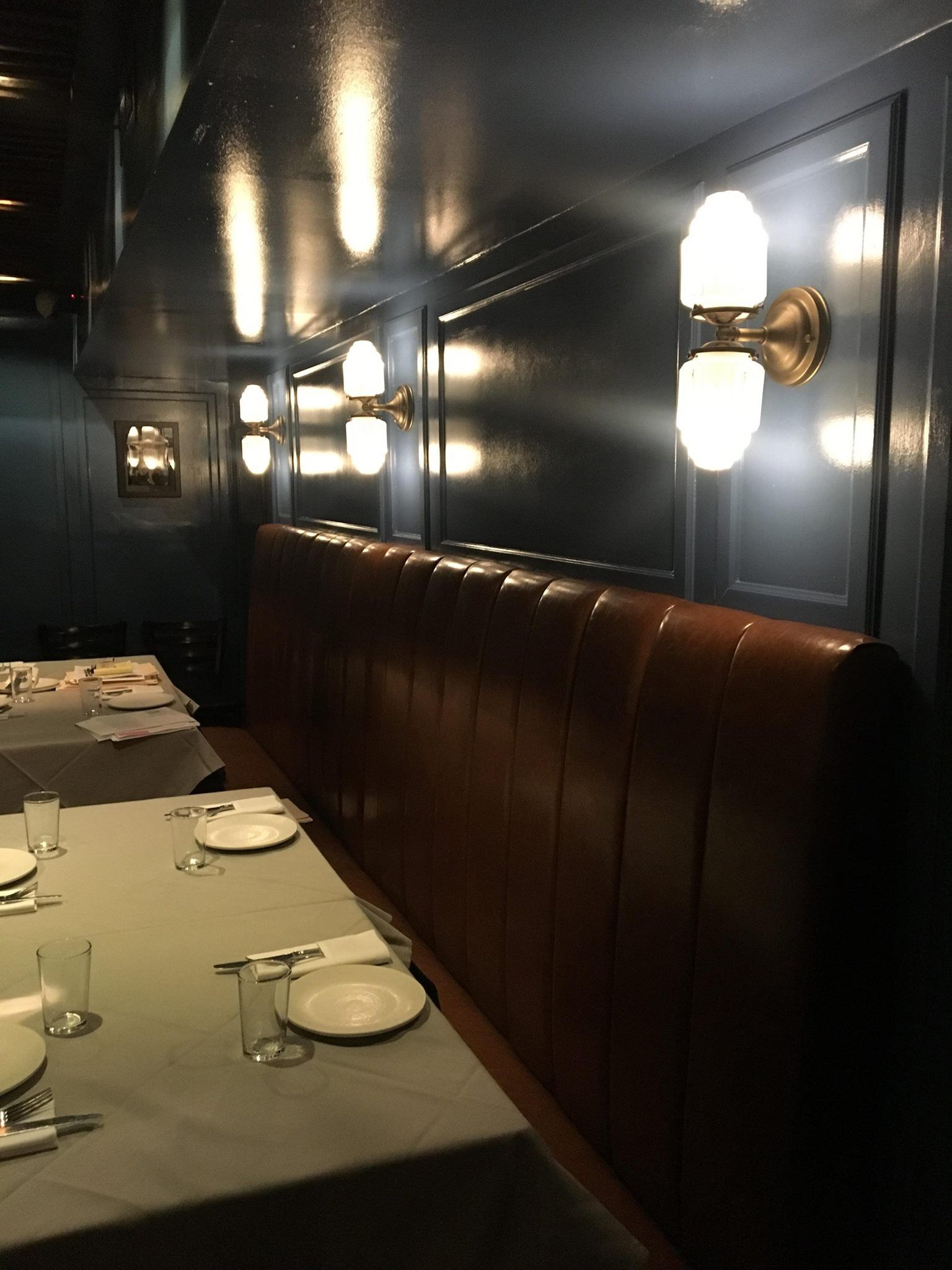 Booth seating in a dimly lit restaurant. Brown leather bench, white tablecloths, sconce lighting.