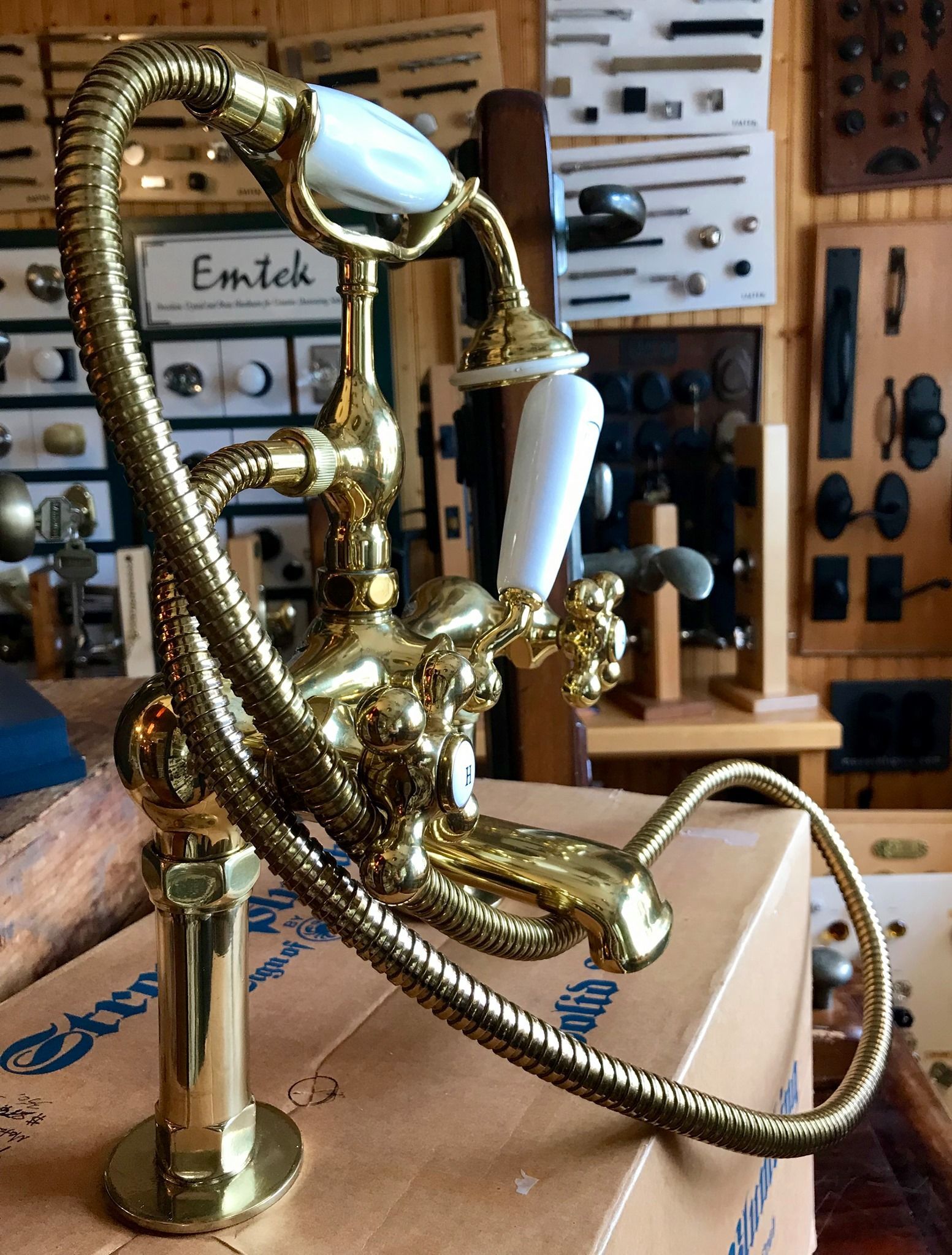 Gold-toned faucet with white handles and a flexible hose, displayed in a hardware store.