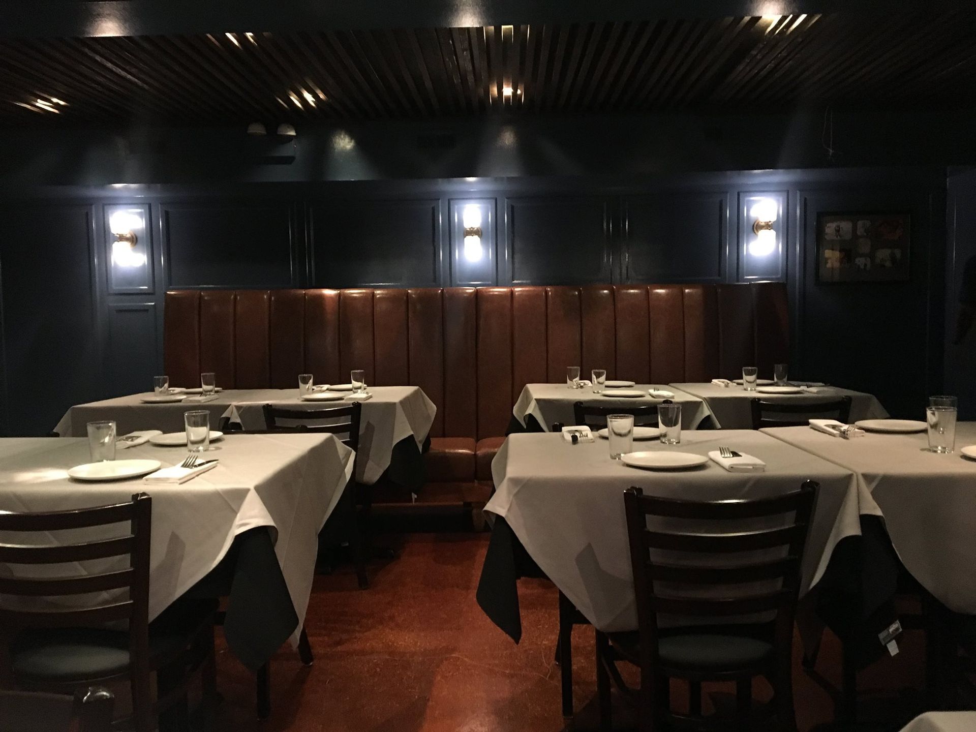 Dark restaurant interior with tables set for dining, and a leather booth.