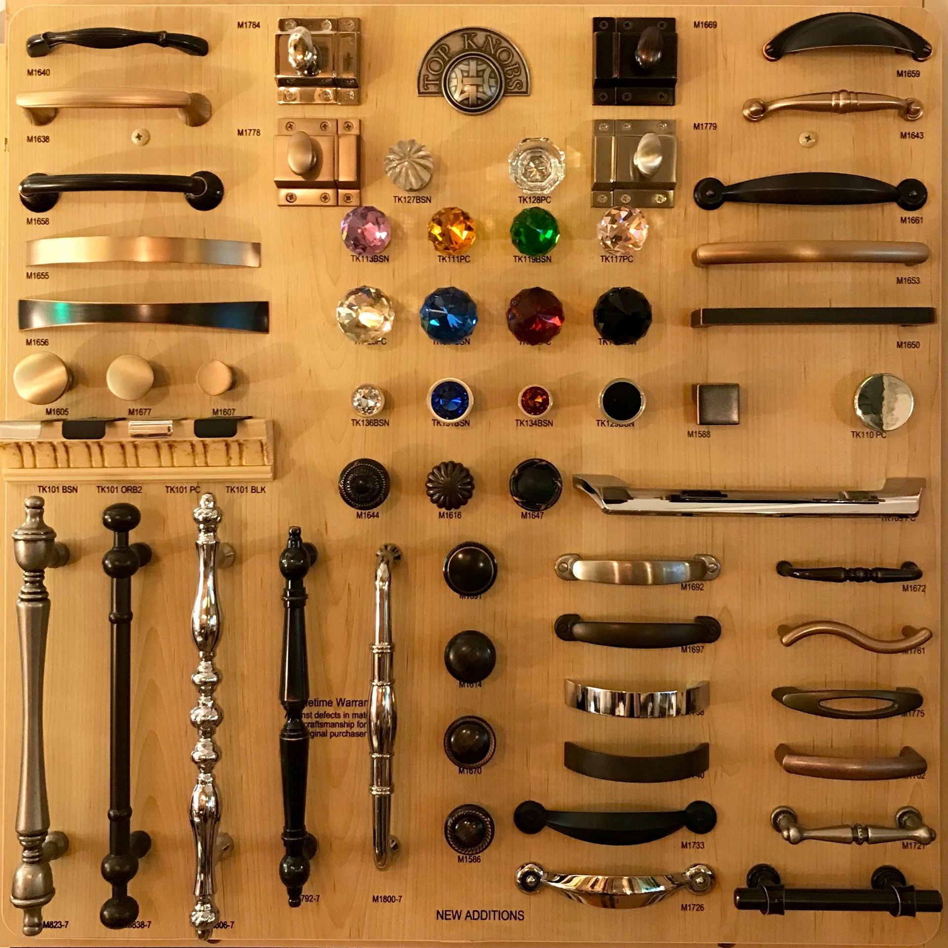 Wooden display board with various cabinet knobs and pulls in different styles and finishes.