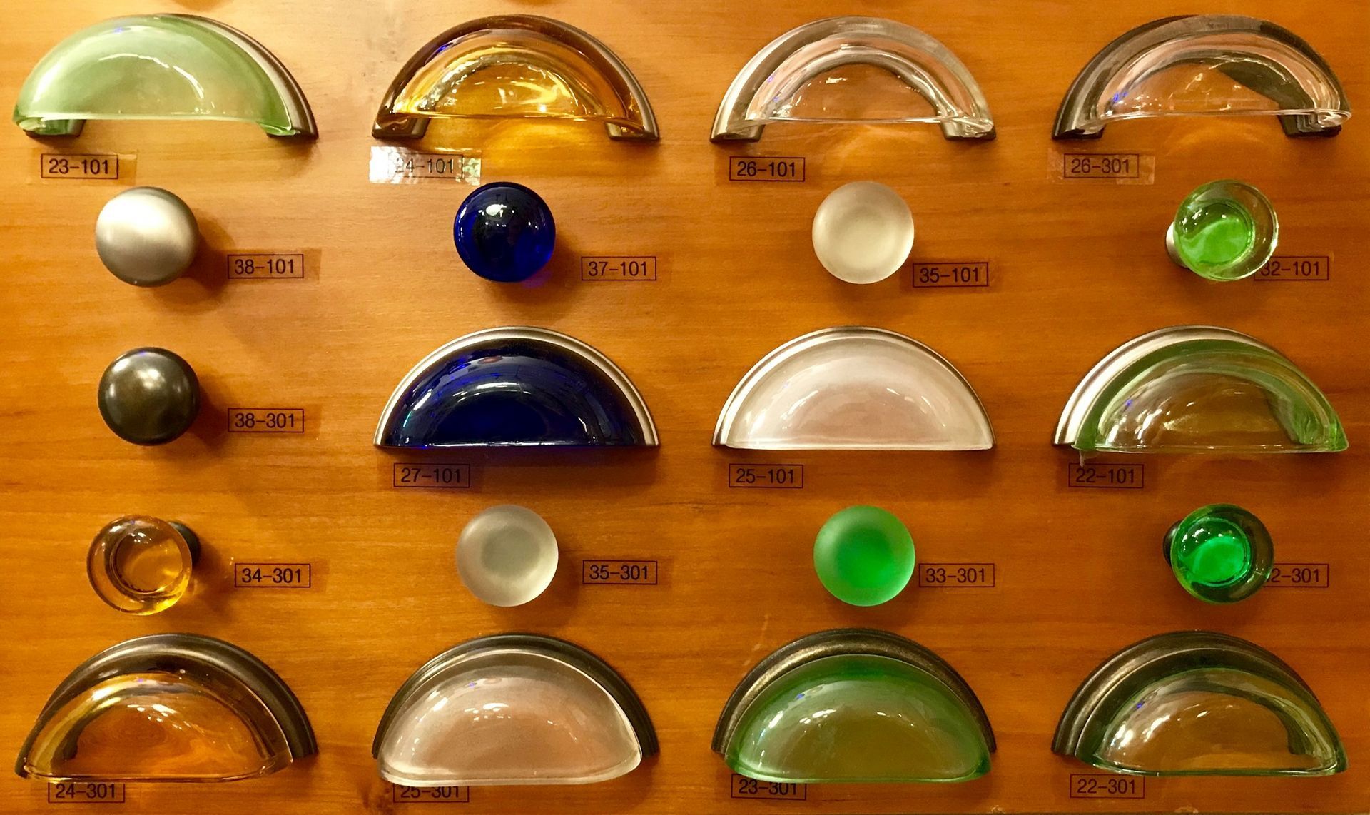 Cabinet hardware display: Various colored glass and metal drawer pulls and knobs mounted on wood.