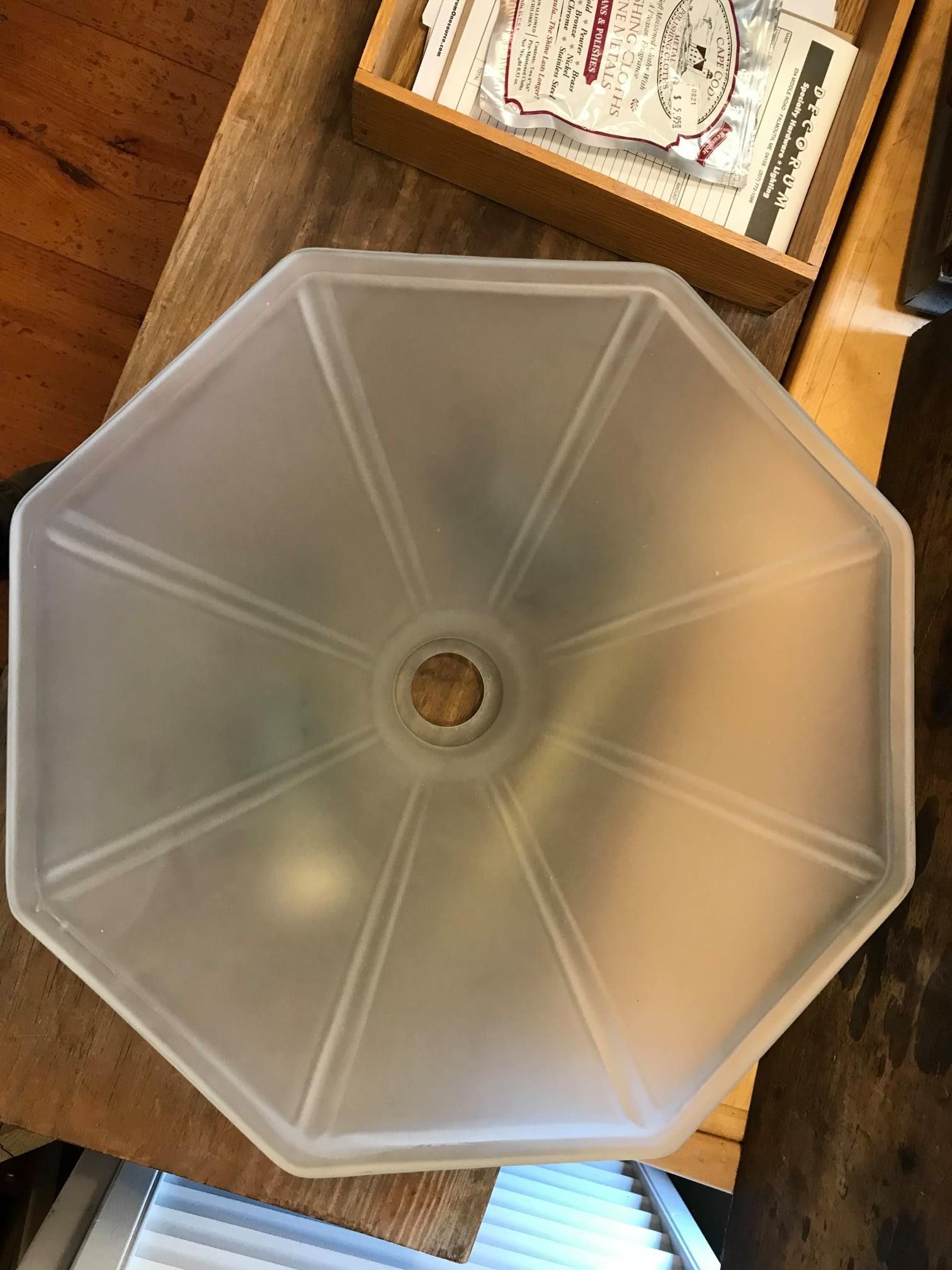 Frosted glass octagon-shaped light fixture, with radial grooves, on a wooden surface.