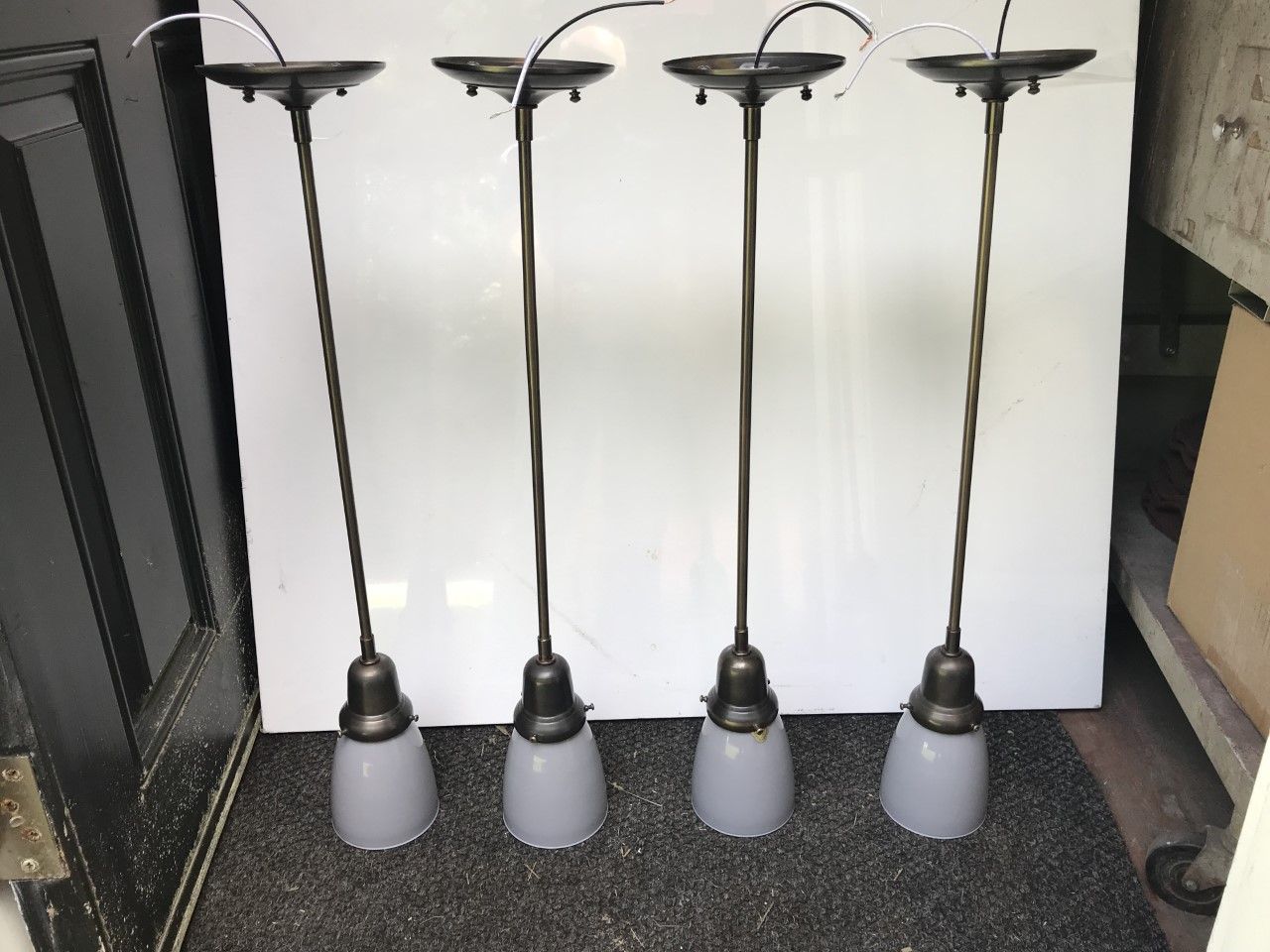 Four bronze-toned pendant lights with white, bell-shaped glass shades, arranged against a white backdrop.