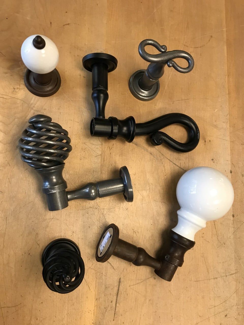 Close-up of various antique door handles on a wooden surface. Designs include ceramic, twisted metal, and spiral styles.