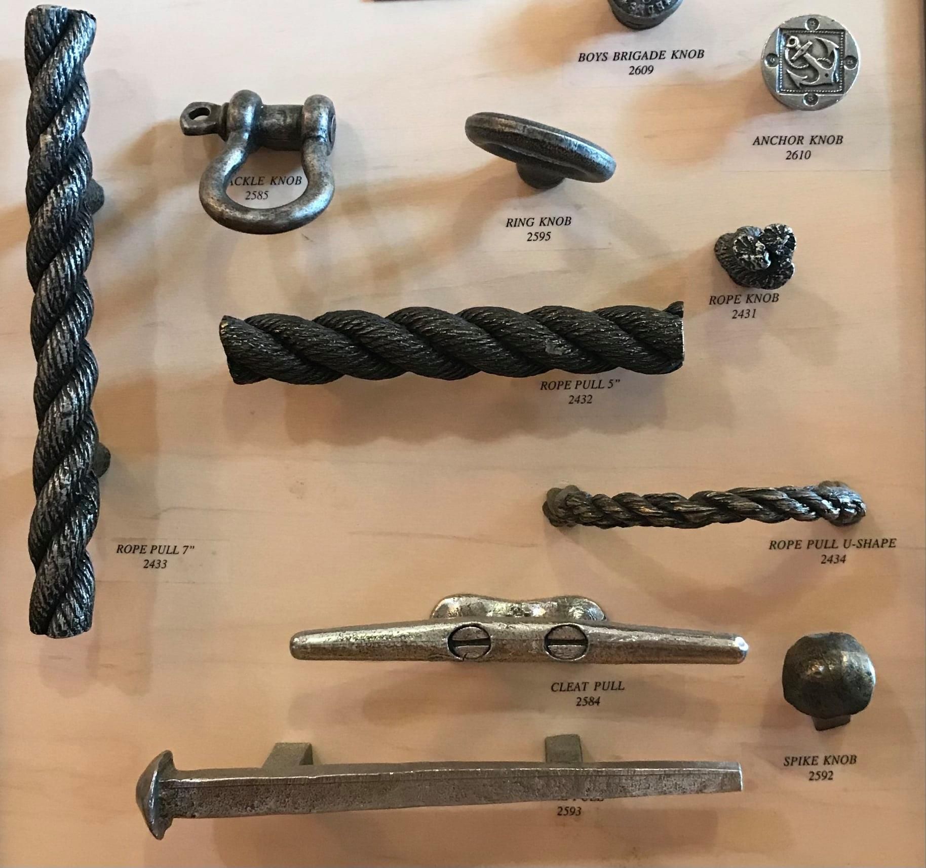 Display of metal hardware, including rope-textured handles and nautical-themed knobs, on a wooden surface.