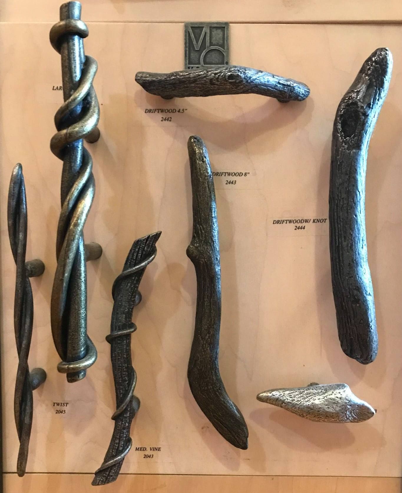 Display of various metal door pulls with natural, organic designs on a wooden backing.