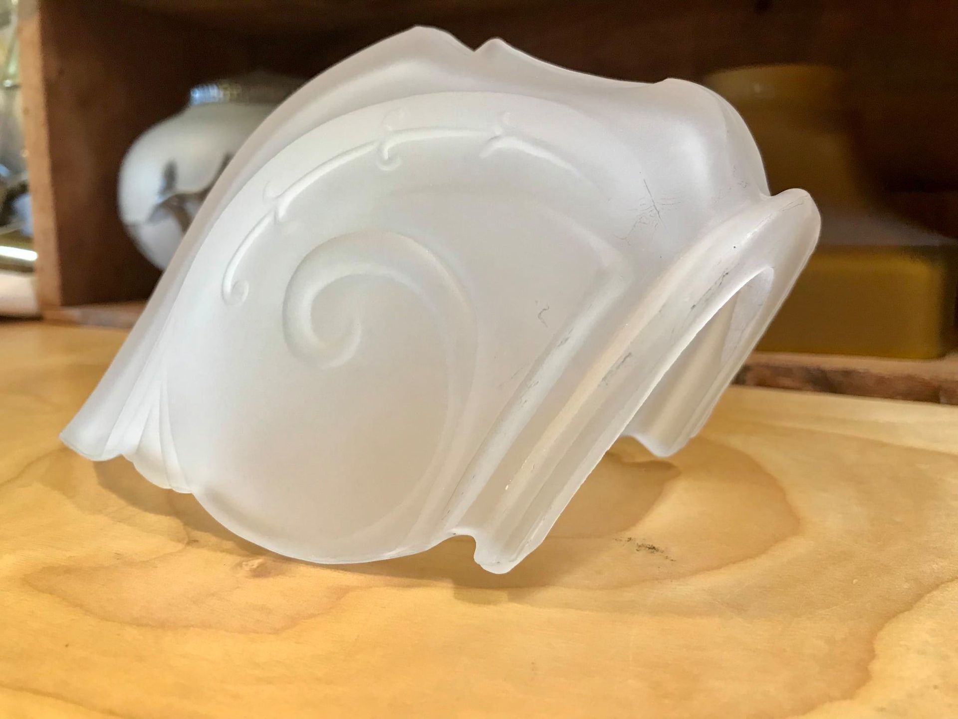 Frosted glass lampshade with swirling floral design, resting on a wooden surface.