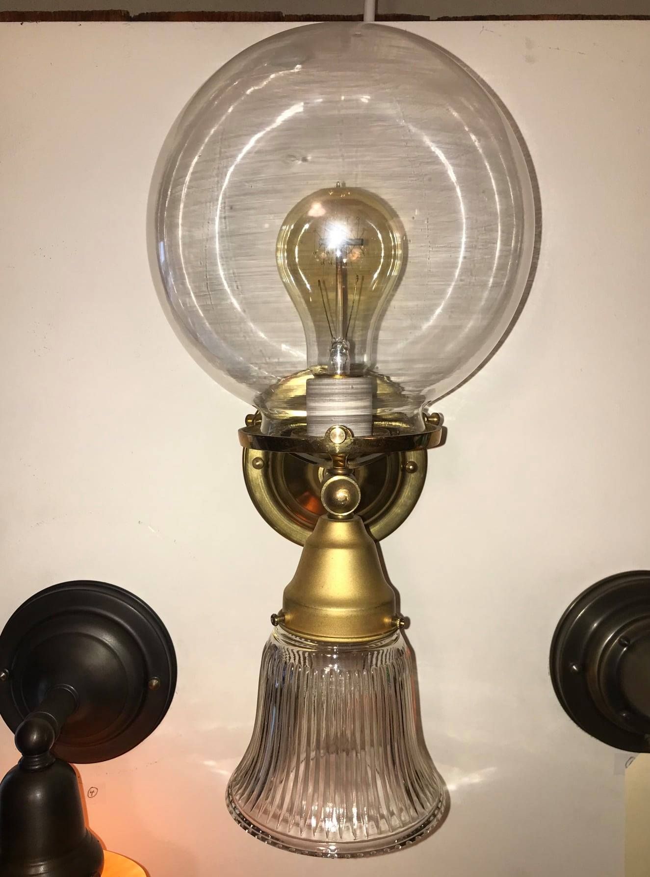 Wall-mounted light fixture with a clear glass shade and a decorative brass base; bulb is visible.