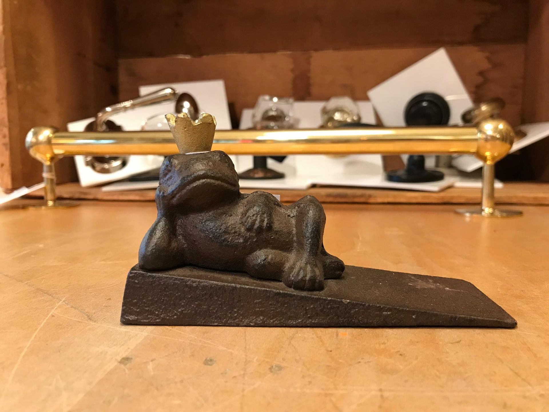 A cast iron frog doorstop wearing a crown, lying on an inclined base.