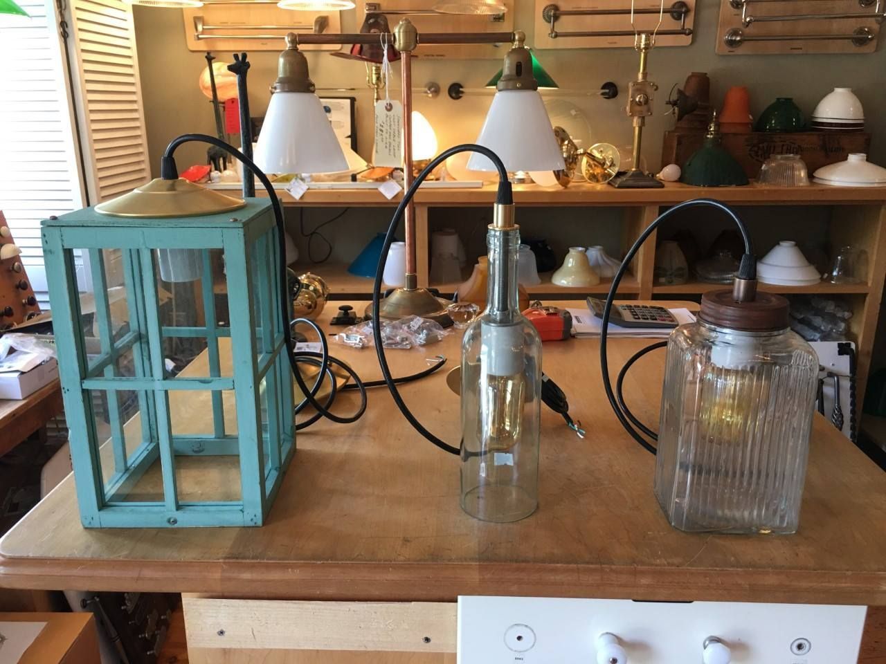 Three unique lamps with glass shades, on a wooden surface, with a teal lantern.