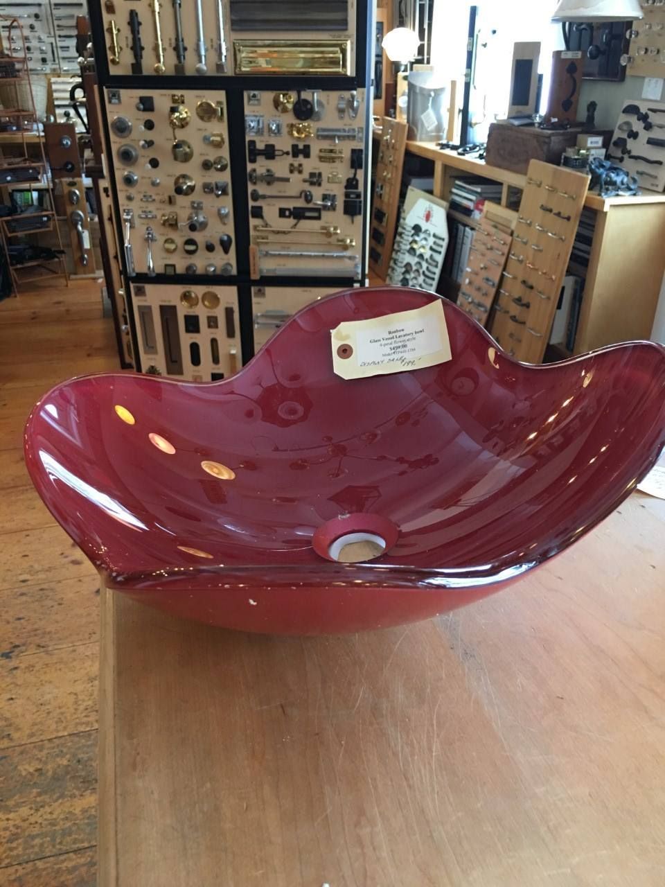 Red glass vessel sink on a wooden surface, with a hardware store background.