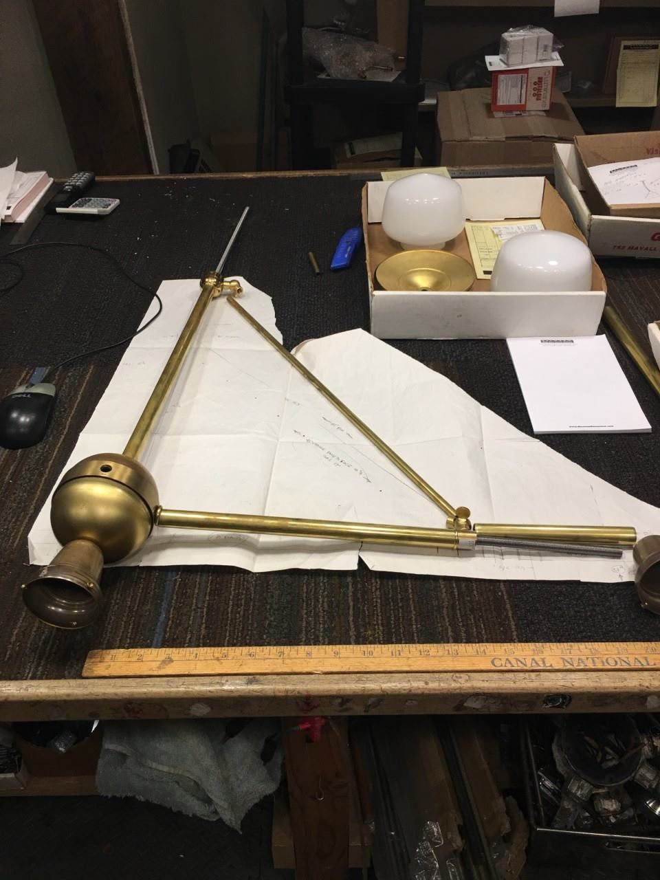 Brass articulated lamp on a table with parts, papers, and tools.