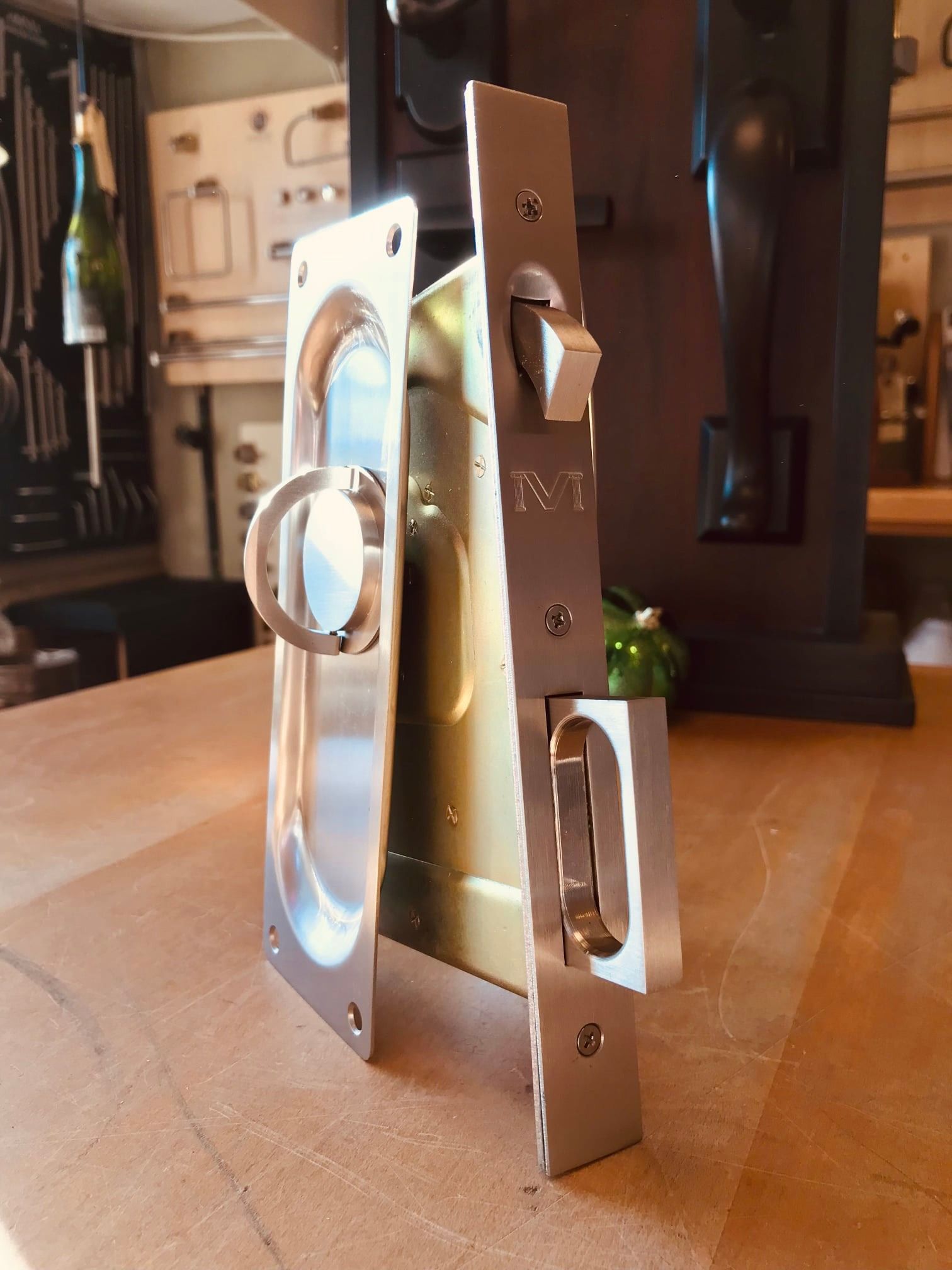 Brushed silver pocket door hardware set; handle and locking mechanism, on a wooden surface.