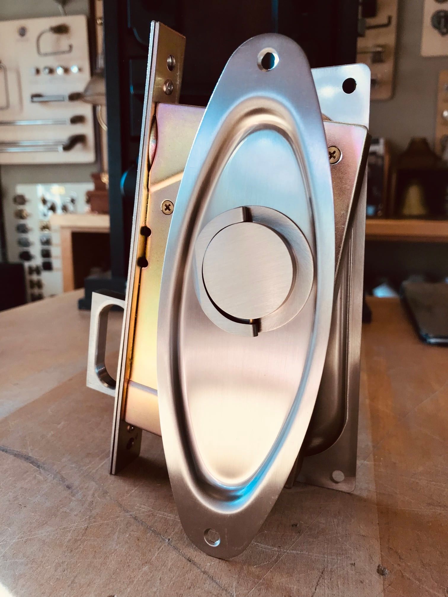 Silver-colored door lock mechanism with an oval-shaped plate, mounted on a wooden surface.