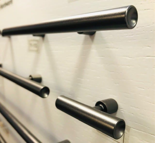 Close-up of several cylindrical, dark metal cabinet handles mounted on a white surface.