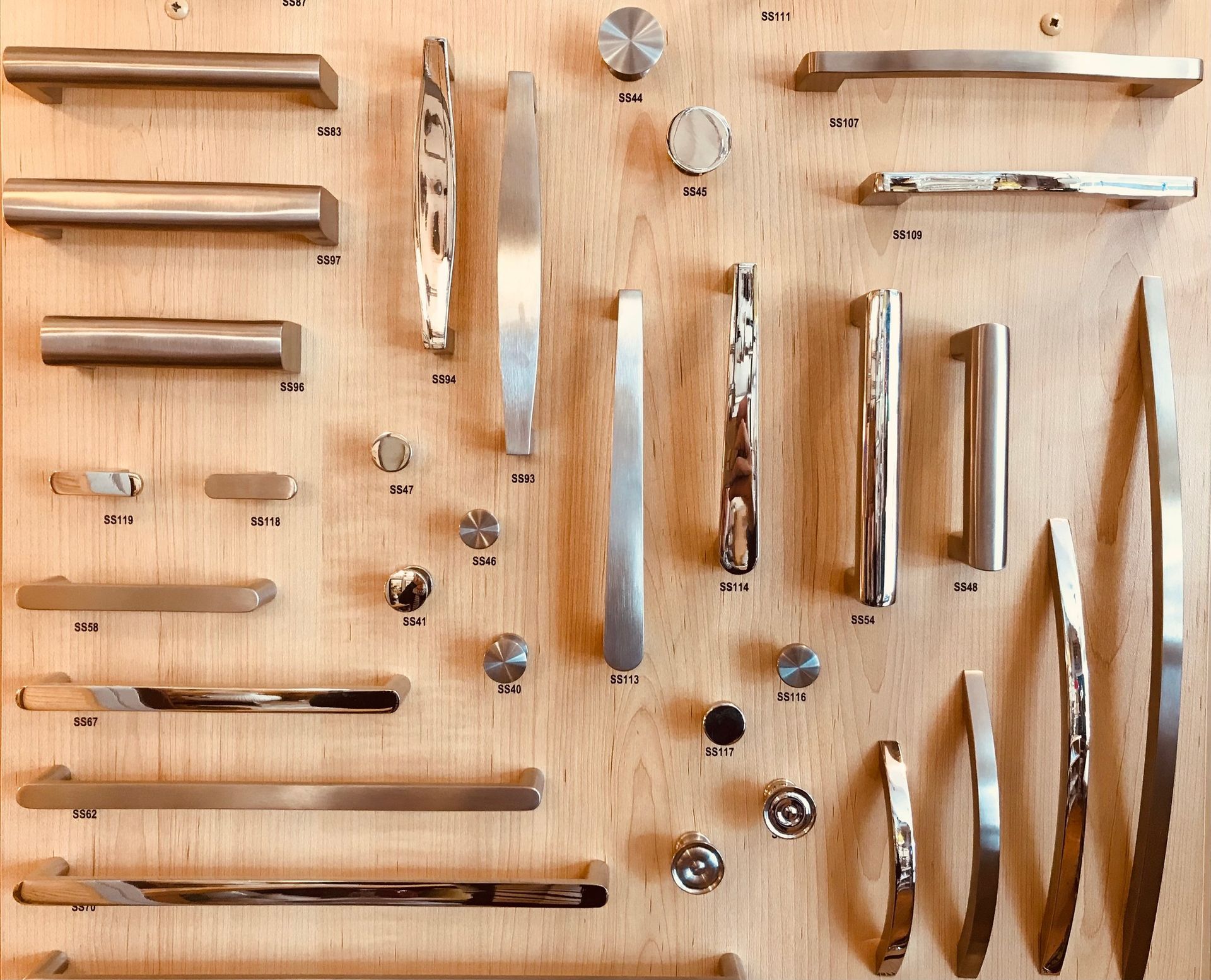 Cabinet hardware samples mounted on a wooden board; various shapes, sizes, and metallic finishes.