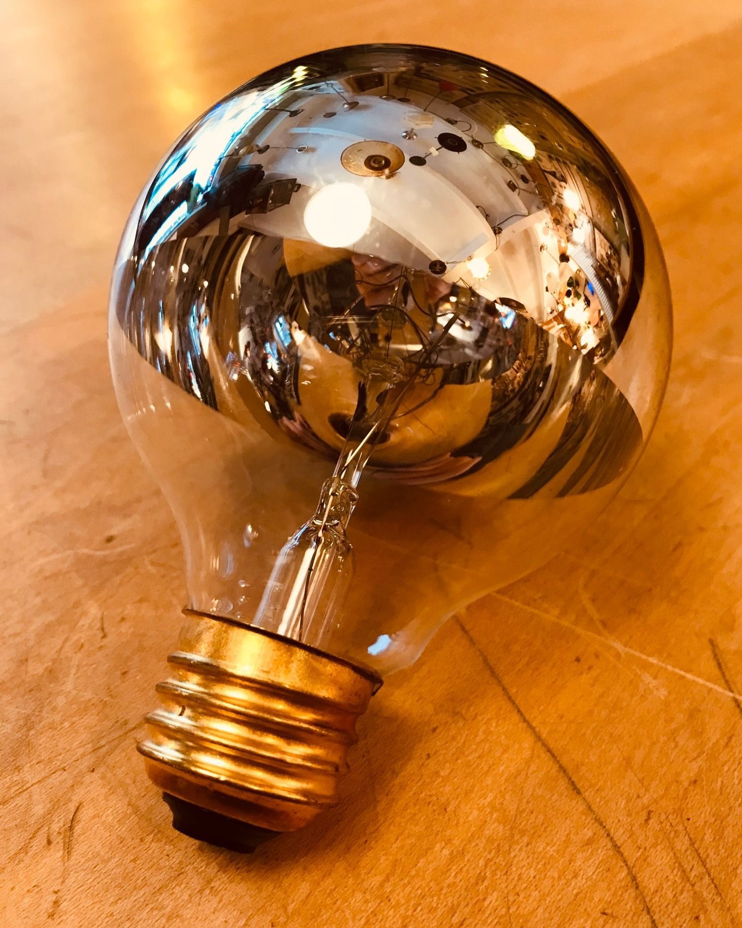 Silver-topped lightbulb on a wood surface, reflecting surrounding objects.