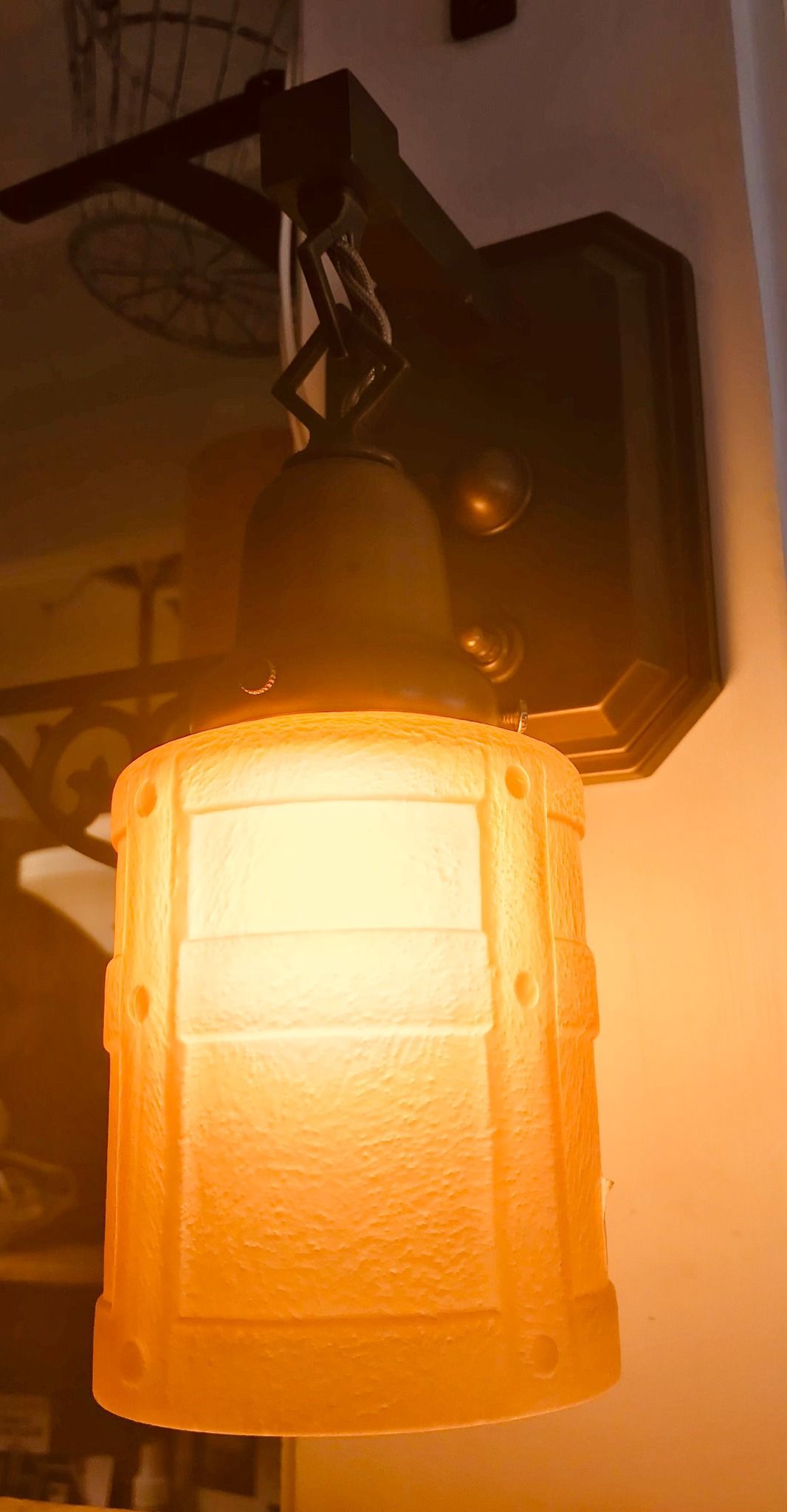 Wall-mounted light fixture with amber-colored, textured glass shade, casting a warm glow. Black metal hardware.