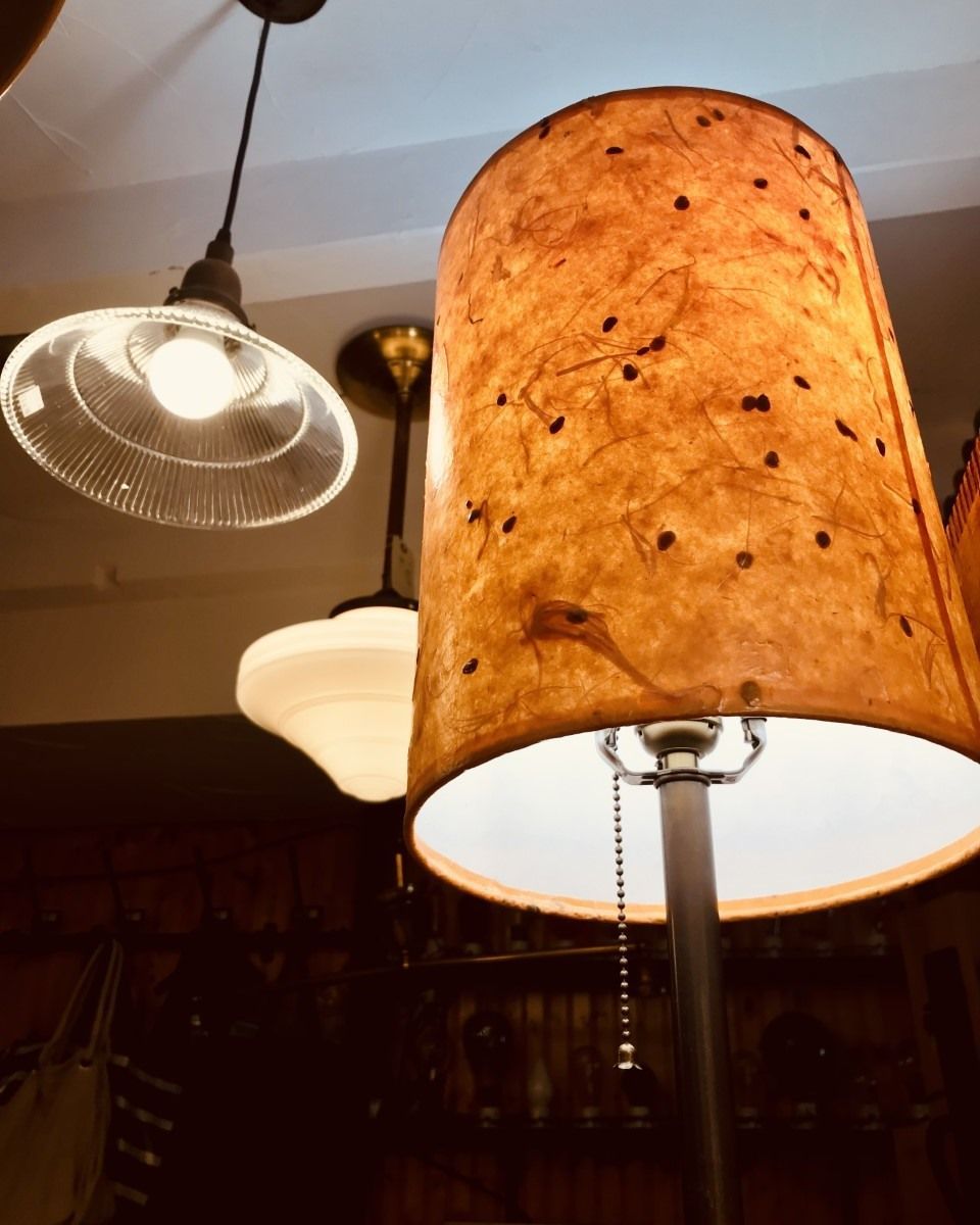 A floor lamp with a textured lampshade is lit, with other ceiling lights in the background.