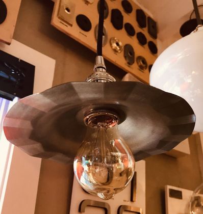 A pendant light fixture with a decorative, fluted metal shade and exposed lightbulb hanging indoors.