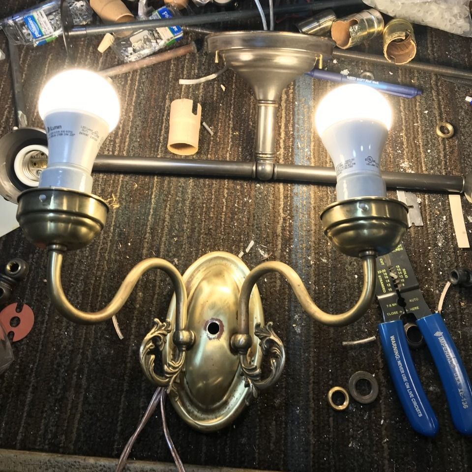 Brass two-bulb wall sconce fixture with exposed wiring, and tools on a dark surface.
